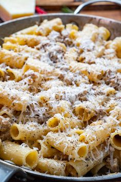 a skillet filled with pasta and meat covered in cheese on top of a wooden table