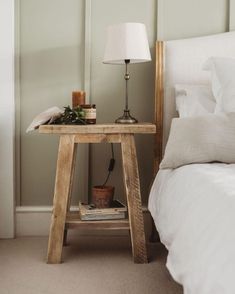 a small wooden table sitting on top of a bed next to a night stand with a lamp