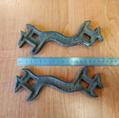 two old metal handles are sitting on a wooden table next to a measuring ruler that shows the length