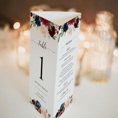 a table number card with flowers on it sitting on a table next to some candles