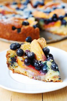 a close up of a slice of cake on a plate with blueberries and peaches