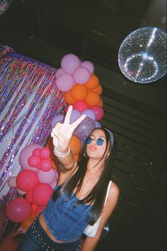 a woman standing in front of a bunch of balloons and pointing up her peace sign