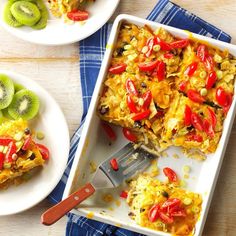 a casserole dish with red peppers and kiwis on the side next to two plates