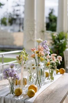 flowers and lemons are arranged in glass vases on a long table with white linen