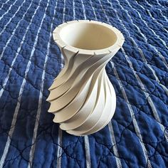 a white vase sitting on top of a blue bedspread covered in striped material