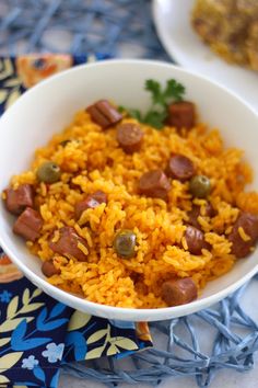 a white bowl filled with rice and sausages on top of a blue table cloth