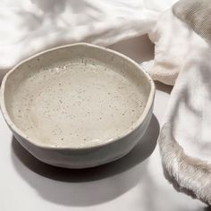 a white bowl sitting on top of a table next to a cloth covered napkins