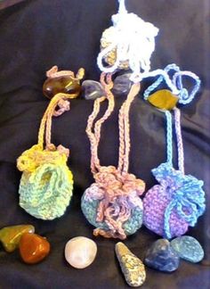 three crocheted items sitting on top of a black cloth covered table next to rocks and seashells