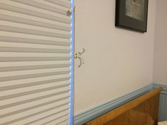 the corner of a room with a window covered in blinds and a framed picture on the wall