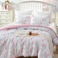 a white bed with pink and blue floral comforter set on it's side