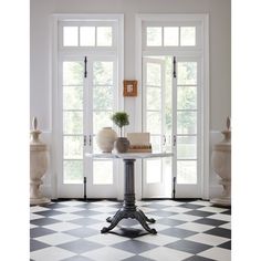 a black and white checkered floor with vases on the table in front of two windows