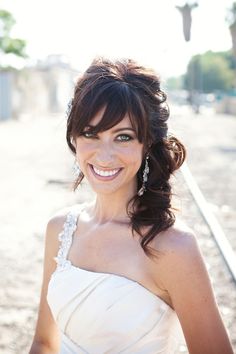 a woman in a white dress standing on train tracks with her hair up and smiling at the camera