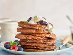 a stack of pancakes topped with ice cream and berries on a blue plate next to a cup of coffee