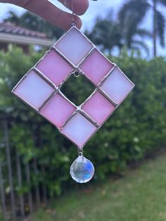 a person holding up a pink and white square shaped glass piece with a drop hanging from it