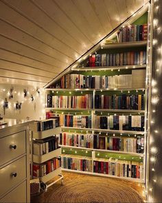 a room filled with lots of books under a slanted ceiling covered in fairy lights