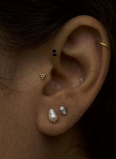 a woman with three different piercings on her ear and behind the ear is a white pearl