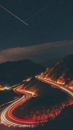 the night sky is filled with stars and light streaks as cars drive along a winding road