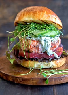 a sandwich with meat, lettuce and tomato on a wooden board sitting on a table