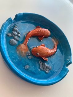 two fish in a blue bowl with rocks and water