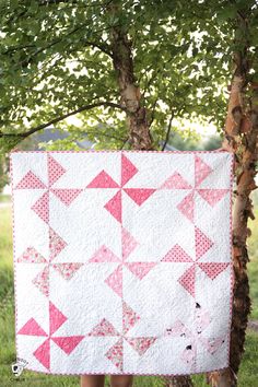 a woman standing next to a tree with a pink and white quilt hanging from it