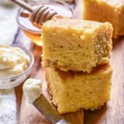 two pieces of cake sitting on top of a wooden cutting board next to honey dips