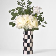 a vase filled with white flowers and greenery on top of a checkered table