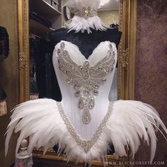 a white corset with feathers and jewels on display in front of a mirror