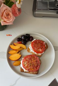 two pieces of bread with tomatoes, cheese and olives on it next to some fruit