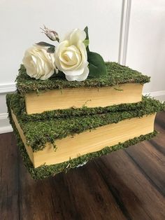 two books stacked on top of each other covered in moss with flowers sitting atop them