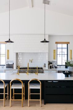 a kitchen with black and white counters, gold accents and hanging lights over the island