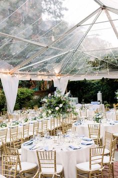 the tables are set up for a wedding reception under a tent with white linens and greenery