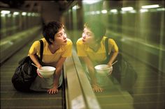 two people sitting on an escalator looking at each other with bowls in their hands