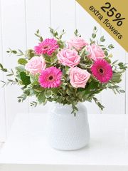 a white vase filled with pink flowers on top of a table