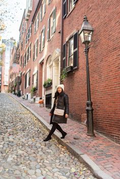 a woman is walking down the street in front of a lamp post and brick building