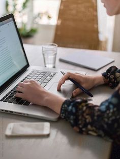 a woman sitting at a table with a laptop and pen in front of her computer