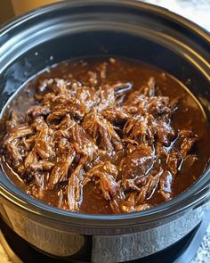 a slow cooker filled with shredded meat in brown gravy on top of a table