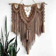 a wall hanging made out of wood sticks and tassels with plants in the background