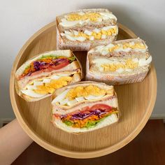 four sandwiches are arranged on a wooden plate