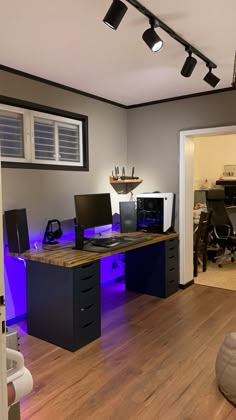 an office with two computers on the desk and blue lights in the room behind it