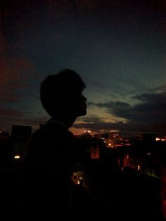 a man standing on top of a roof next to a tall building at night with the city lights in the background