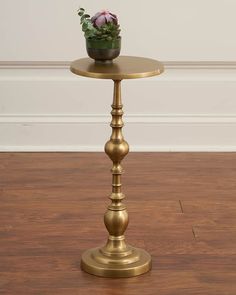 a small gold table with a potted plant on it's top and wood flooring