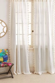 a chair sitting in front of a window next to a white curtain with pom - poms on it