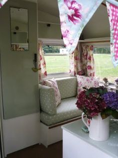 the inside of a camper with flowers and curtains hanging from it's windows