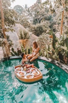 a woman sitting on top of a wooden boat filled with food next to a pool