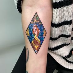 a woman's arm with a stained glass mermaid tattoo on the left inner arm