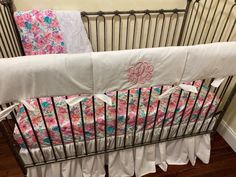 a baby crib with pink and blue floral bedding, white ruffles, and monogrammed sheets