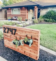 a wooden sign with plants on it in front of a house that has the number 477 written on it