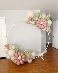 a white circle with balloons and flowers on the top is in a room that has wood floors