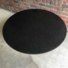 a black round table sitting on top of a sidewalk next to a brick wall and door