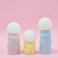 three different colored vases with white and blue balls in them on a pink background